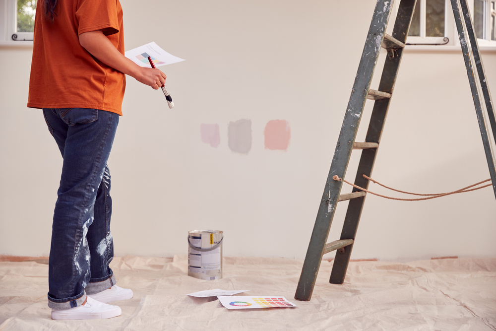 Close-up view of a woman applying test paint swatches on the wall while decorating a room in a new home, considering the balance between paint color and natural light